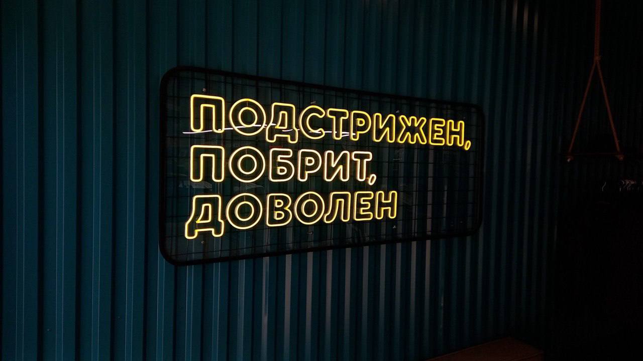 Жёлтая неоновая вывеска «Подстрижен, побрит, доволен» в барбершопе